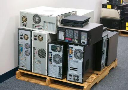 Pile of assorted desktop PC towers stacked on wooden pallet in warehouse