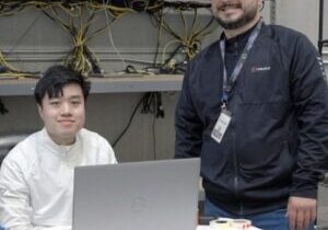 Two technicians smiling at laptop in electronics repair workspace